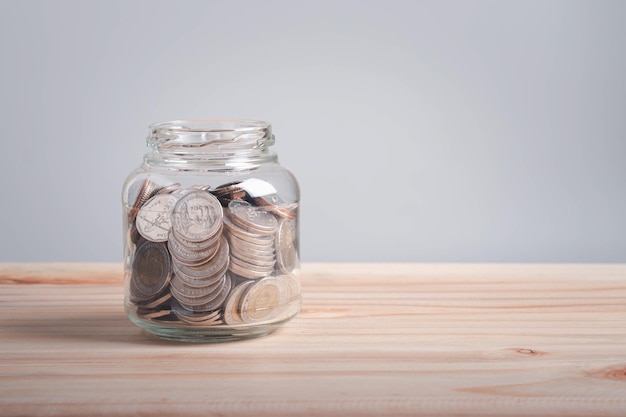 Moneda tailandesa en un tarro de hierba cerrado con una tapa negra sobre un concepto de ahorro de mesa de madera