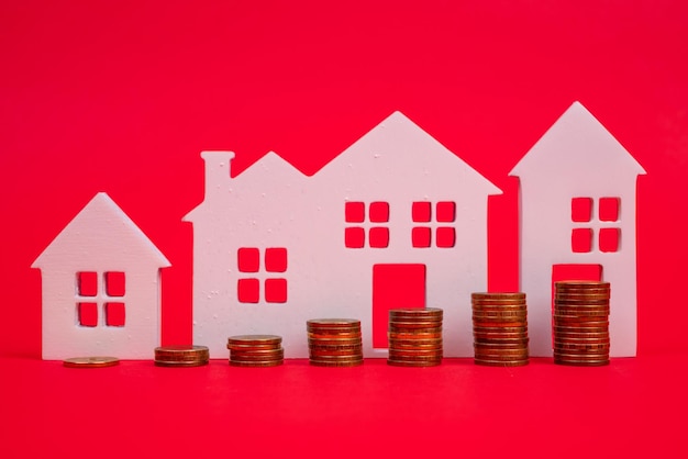 Monedas y casas sobre un fondo rojo El concepto del aumento del precio de los bienes raíces