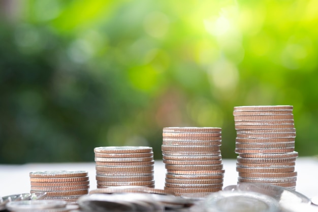 Monedas crecientes del primer que apilan con el fondo y la luz del sol del verdor.