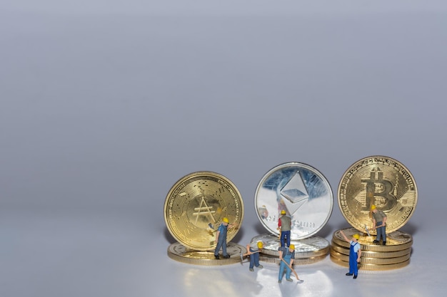 Monedas criptográficas valiosas bitcoin ether y ada en una fila con muchos trabajadores sobre fondo gris vista inferior derecha