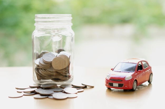 Monedas en un frasco por el coche de juguete en la mesa