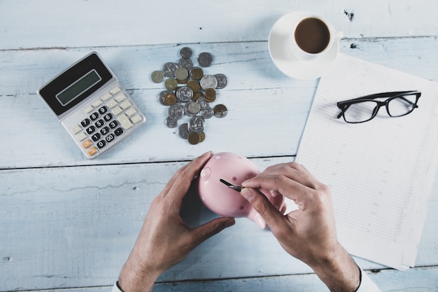 Monedas de mano de hombre y hucha con calculadora sobre la mesa