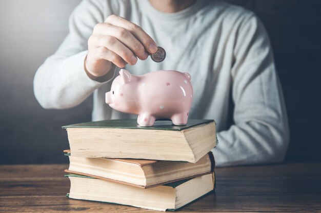 Monedas de mano de hombre con hucha en el libro en el escritorio