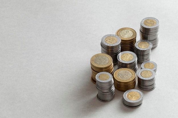 Monedas de pesos mexicanos de diferentes denominaciones apiladas en una mesa con espacio para copiar