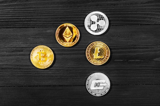 Monedas de plata y oro con bitcoin, rizo y símbolo etéreo sobre madera.