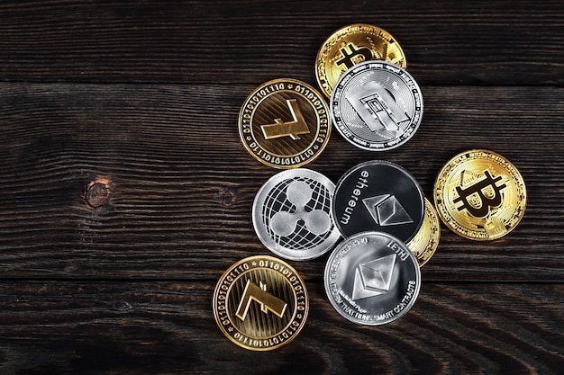 Monedas de plata y de oro con el símbolo del bitcoin, de la ondulación y del ethereum en el fondo de madera.
