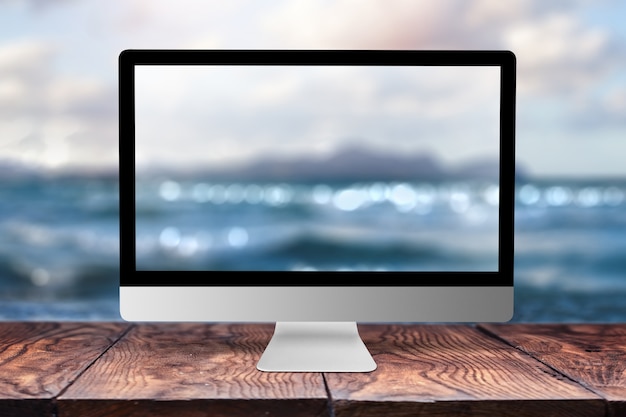 Monitor de computadora con mar imagen borrosa sobre una mesa de madera contra el mismo con bokeh, copie el espacio. Trabajando de forma remota en la costa, en la naturaleza, fuera del concepto de oficina.