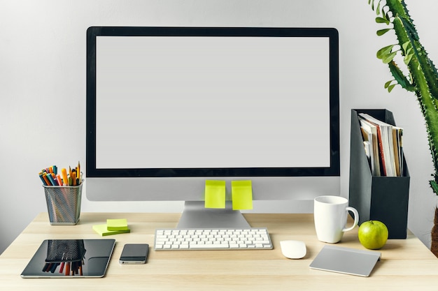 Monitor de computador com tela branca de maquete na mesa de escritório com suprimentos