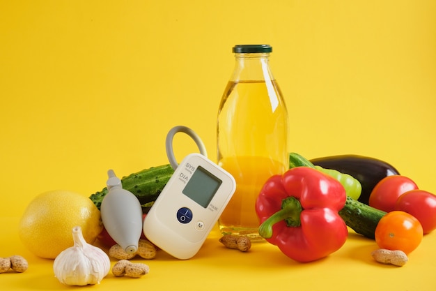 Monitor de óleo vegetal, vegetais e pressão arterial em um fundo amarelo. nutrição e dieta para hipertensão e doenças cardíacas