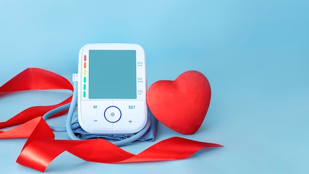 Monitor de pressão arterial com fita de seda vermelha e figura de coração vermelha sobre fundo azul