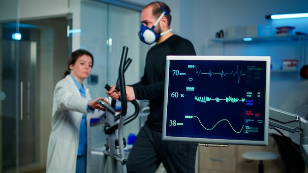 Foto monitor mostra leitura de ekg de atleta homem correndo no cross trainer e discutindo com pesquisador médico