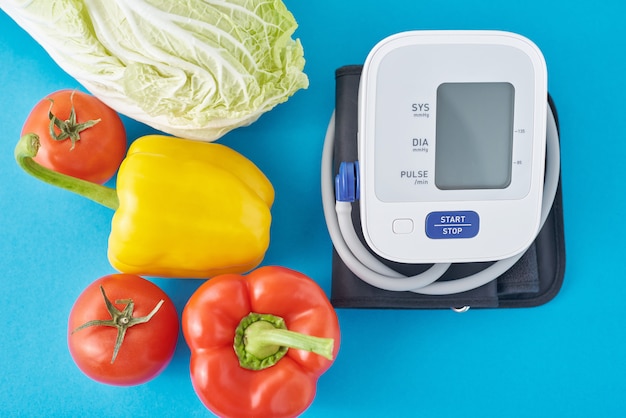 Monitor de presión arterial digital y verduras frescas sobre fondo azul. Concepto de salud