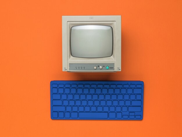 Monitor vintage y teclado azul sobre un fondo naranja. Equipo retro. Endecha plana.