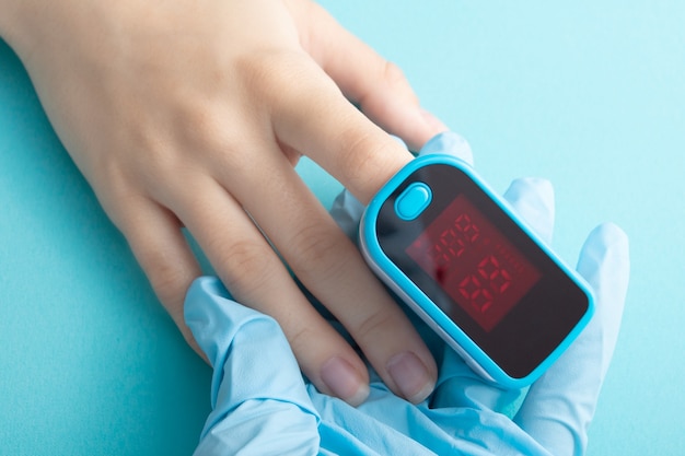 Monitorando a saturação de oxigênio do sangue com um dispositivo especial em um dedo feminino sobre fundo azul