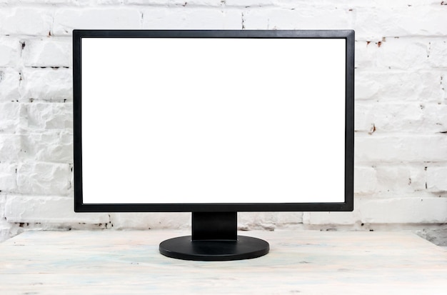 Monitoreo de computadora en una mesa contra la pared de ladrillo pantalla blanca en blanco