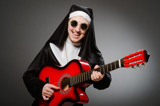 Monja divertida con guitarra roja tocando.