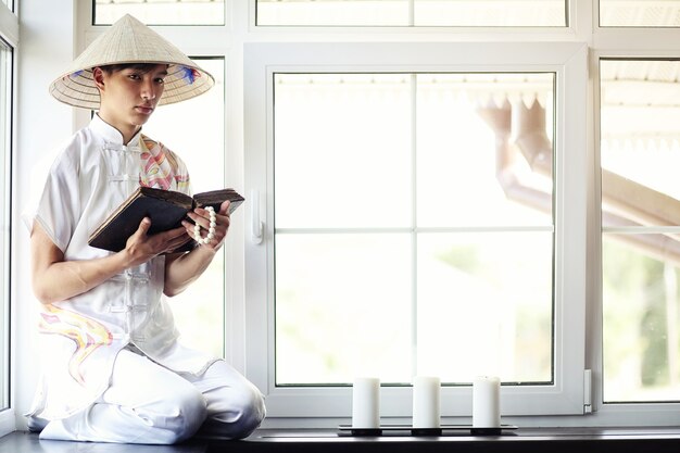 Monje asiático en kimono leyendo un libro viejo