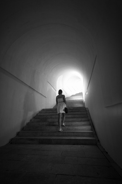 Monochrome erschossene Frau, die die Treppe am Tunnel mit Licht am Ende hinaufgeht