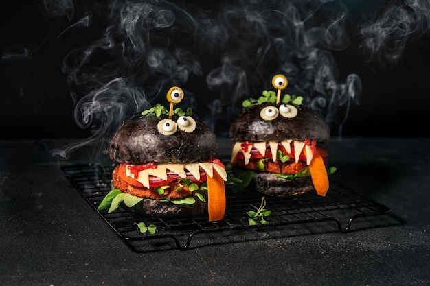 Foto monster-sandwiches mit schwarzem brötchen, veganem patty-käse, olivenaugen und rauch auf dem schwarzen hintergrund halloween-burger