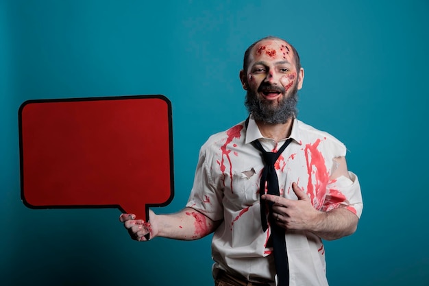 Monstruo aterrador sosteniendo una burbuja de voz de maqueta, mostrando un mensaje de texto en una caja de cartón aislada. Cerebro comiendo zombie espeluznante con cicatrices y heridas sangrientas haciendo publicidad en el estudio.