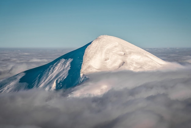 Montaña coronada de nieve por encima de las nubes. Monte Goverla en las montañas de los Cárpatos