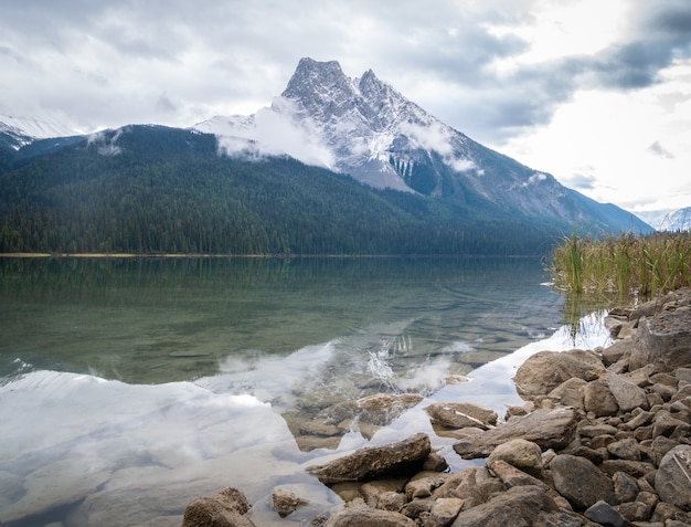 Montaña envuelta en nubes reflejadas en tranquilas aguas del lago verdoso