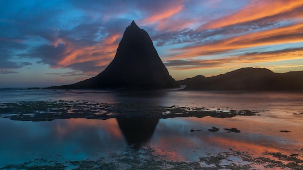 una montaña está en el agua con una puesta de sol en el fondo