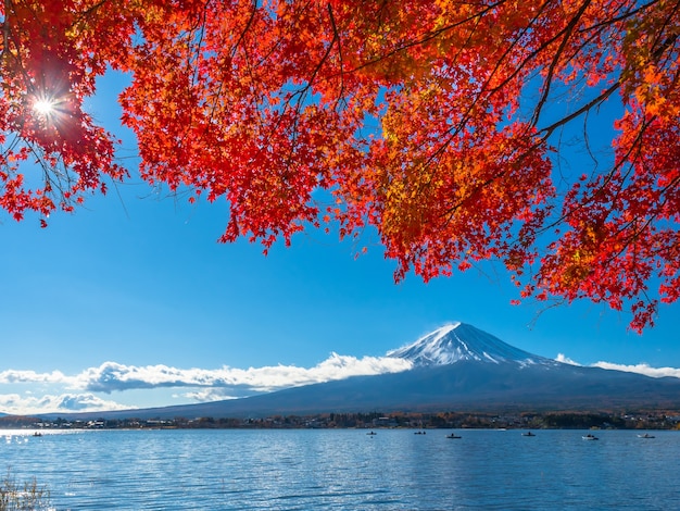 Montaña de Fuji con la hoja de arce roja en los barcos del primero plano y de navegación en el lago.