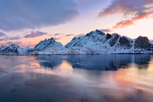 Una montaña nevada con un cielo morado y el sol reflejado en el agua