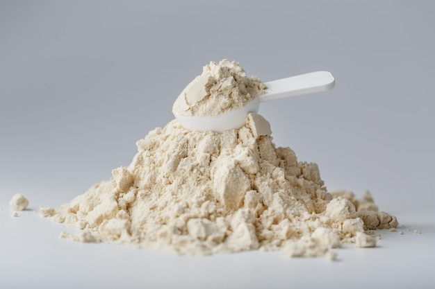 Una montaña de proteína de soja aislada en polvo con una cuchara dosificadora sobre un fondo blanco.