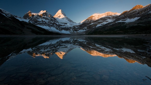 una montaña se refleja en un lago con el sol poniéndose detrás de ella