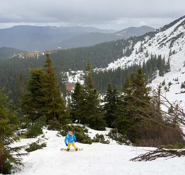 Foto montañas boscosas de invierno freeriding masculino en snowboard campiña montañosa para snowboard y esquí de travesía