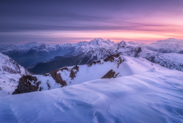 Montañas cubiertas de nieve y colorido cielo púrpura con nubes al atardecer en invierno Hermoso paisaje invernal con rocas nevadas y colinas al atardecer Paisaje con alpes en la noche helada Montañas alpinas