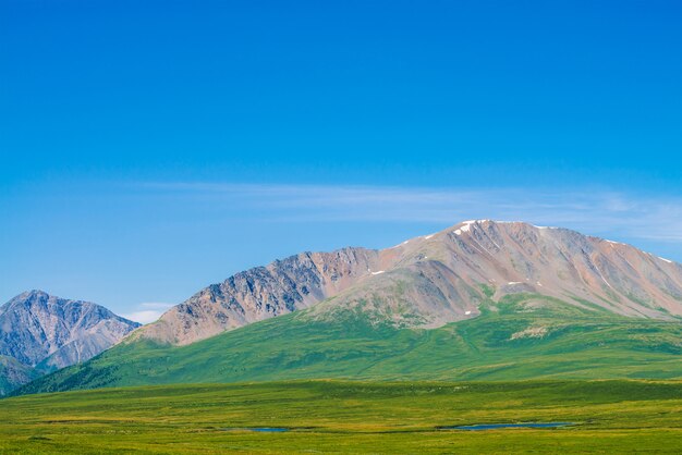 Montañas gigantes con nieve sobre el valle verde bajo el cielo azul claro.