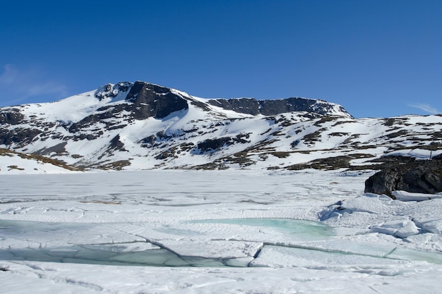 Montañas nevadas con lago congelado y cielo azul, noruega