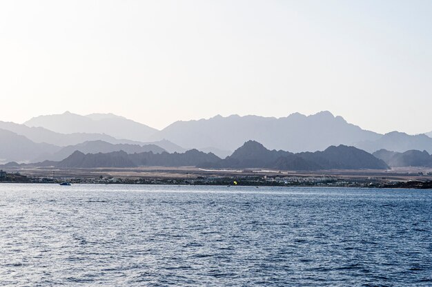 Montañas en la niebla en la playa. Vista desde el agua. Paisaje de verano con mar y cordillera.