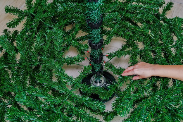 Montando a árvore de Natal dentro de uma casa. Mão feminina adicionando galhos artificiais para moldar em um suporte