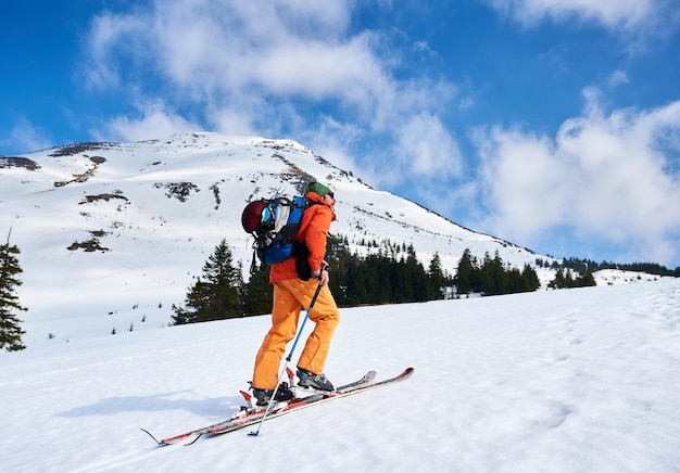 Montañero caminando por una cresta nevada con los esquís en la mochila en un día soleado