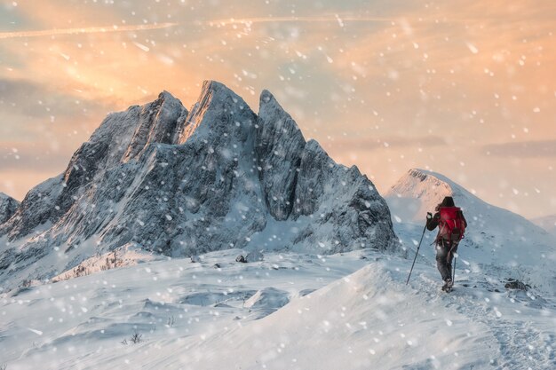 Montañero mochilero senderismo en la colina de nieve con majestuoso monte con nevadas en la mañana. Pico Segla, Noruega