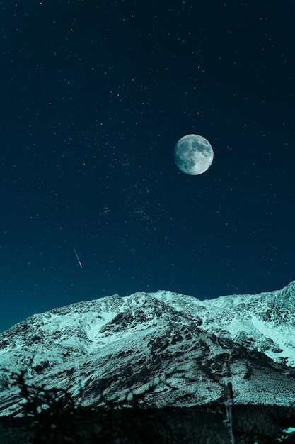 Montanha com neve à noite sob lua cheia e estrelas com fundo