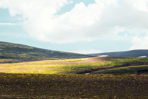 Montanha de musgo resistida com luz solar e céu azul no verão nas terras altas da Islândia