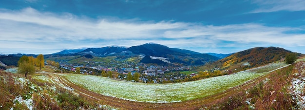 Montanha dos Cárpatos de outubro com primeira neve de inverno em estrada suja e vila no vale