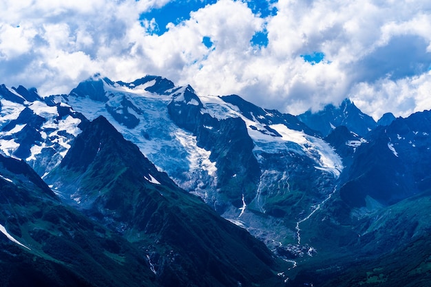 Montanha nevada contra céu nublado De baixo de nuvens brancas flutuando no céu azul sobre o cume da montanha coberta de neve em dia ensolarado na natureza