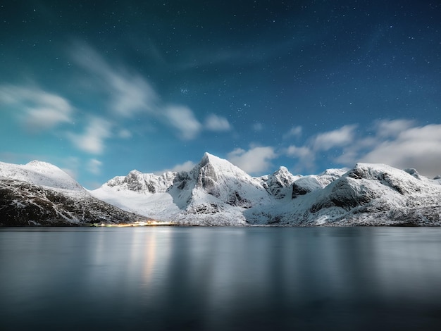 Foto montanhas e reflexos na água à noite paisagem de inverno o céu com estrelas e nuvens em movimento natureza como pano de fundo noruega viagens