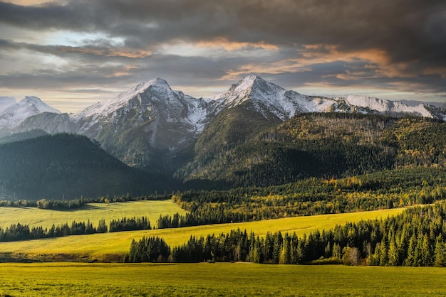 Montanhas Tatra cobertas de neve e folhagem de árvores coloridas e pastagem no outono