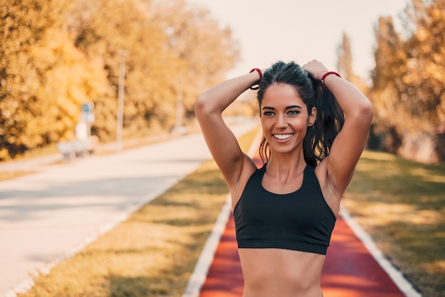 Montar atleta femenina atar el cabello antes de su entrenamiento al aire libre en la pista de atletismo.