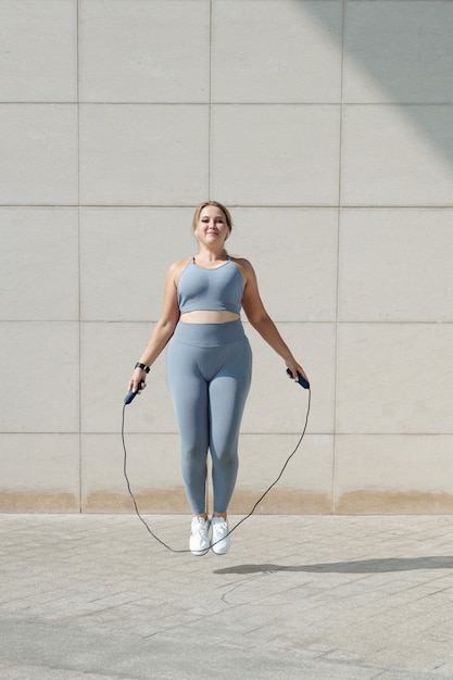 Foto montar mujer joven de talla grande saltando con saltar la cuerda al aire libre para calentar antes de entrenar