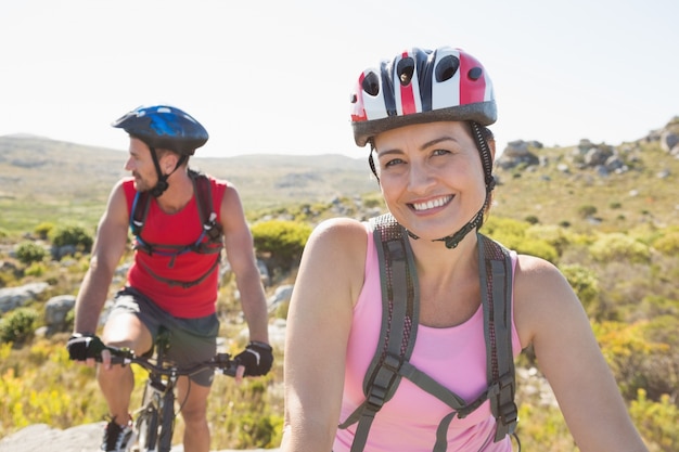 Montar pareja de ciclista sonriendo a la cámara en el sendero de montaña