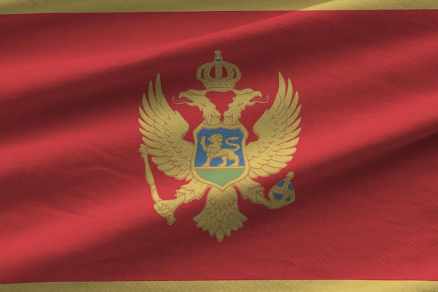 Montenegro-Flagge mit großen Falten, die in der Nähe unter dem Studiolicht im Innenbereich winken Die offiziellen Symbole und Farben im Banner