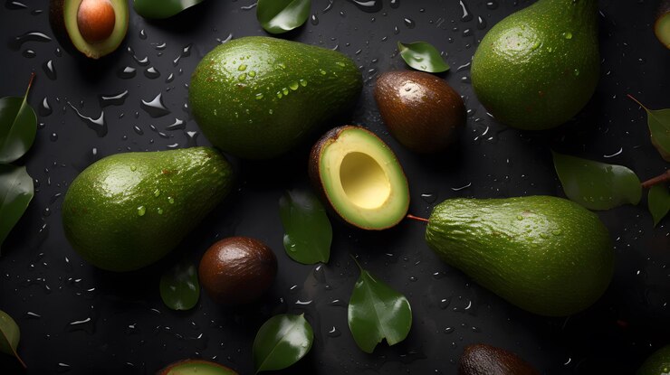 Un montón de aguacates sobre un fondo negro con gotas de agua sobre ellos.